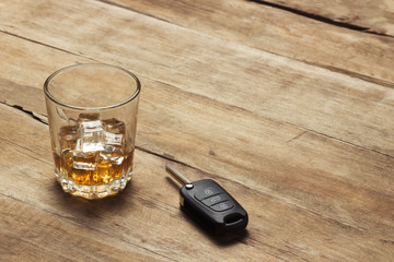 Glass with whiskey and ice and car keys on a wooden background. Drunk driving concept, the risk of drinking and driving, alcohol intoxication.