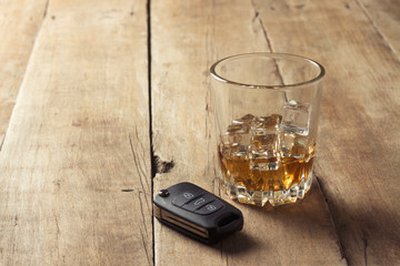Glass with whiskey and ice and car keys on a wooden background. Drunk driving concept, the risk of drinking and driving, alcohol intoxication.