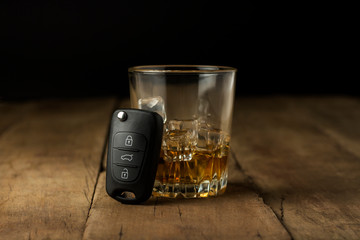 Alcoholic drink with ice in a glass and car keys on a wooden background. Drunk driving concept, stop drinking and driving.
