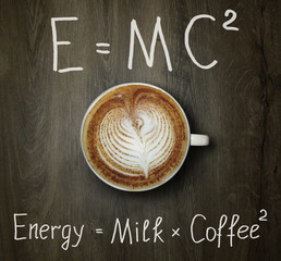 The cup of black coffee with milk and two funny formulas. Wooden background.