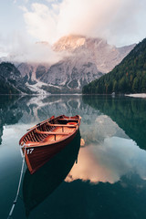 Vertical photo. Wooden boat on the crystal lake with majestic mountain behind. Reflection in the...
