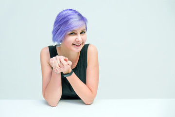 Talk to me - Concept portrait of a beautiful girl with purple hair on a white background sitting at the table and talking.