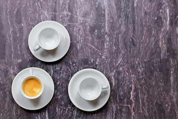 Top view on three little coffee cups on lilac marble background. One with coffee, two others empty. Indoors, copy space.