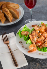 salad with Royal prawns on a white plate on the dark surface of the table with Cutlery.