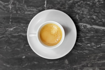Top view on little cup and saucer, with coffee espresso, on black and white marble background. Indoors, copy space.