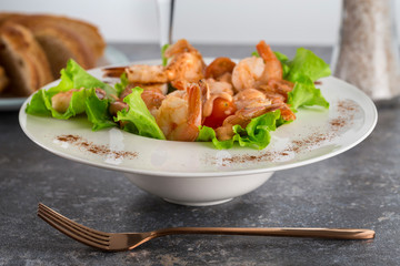 salad with Royal prawns on a white plate on the dark surface of the table with Cutlery.