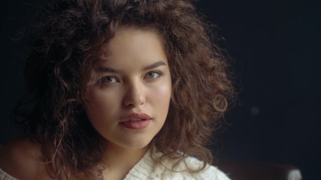Close up video portrait of young beutiful cute curly girl posing on dark background. Natural day light from window