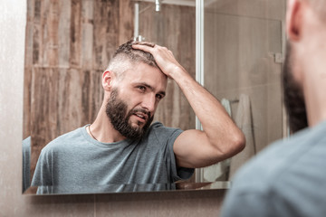 Handsome bearded dark-eyed businessman fixing his hair