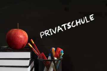 Schulbücher, Stifte, Apfel und eine Kreidetafel mit dem Wort Privatschule