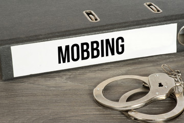 Handschellen und ein Ordner mit dem Aufdruck Mobbing