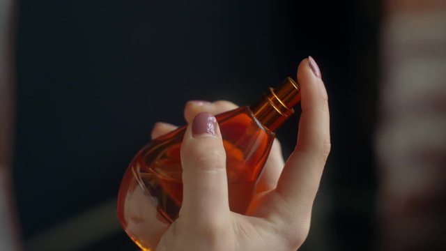 Close up of hand of young fashionable woman holding, spraying, using luxury perfume in orange glass bottle.