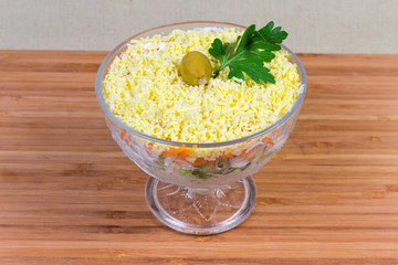 Fish salad mimosa with cheese, eggs, vegetables in glass bowl