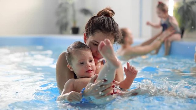 Young mom in the pool playing with her baby daughter in slow motion. Sports family engaged in an active lifestyle