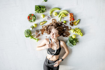 Beauty portrait of a sports woman surrounded by various healthy food lying on the floor. Healthy...