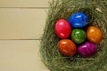 Easter food.multicolored Easter Eggs and  in a hay nest on a yellow wooden board background