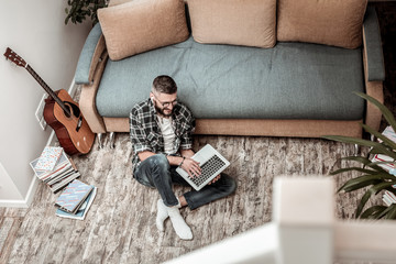 Positive cheerful man typing a text on his laptop