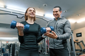 Fototapeta na wymiar Male personal fitness trainer helping young woman to do workout in gym. Sport, athlete, training, healthy lifestyle and people concept