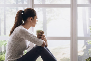 Young woman sitting next to the window and looking away
