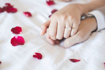 Close up hand groom couple lovers putting wear the Wedding Ring on bride Holding hands together on the bed Sprinkle rose petals Represents romantic. Propose for get marry marriage and love concept.