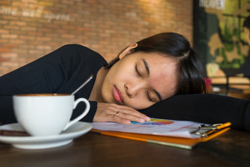 Portrait of a tired young businesswoman sitting at the table, near cup of coffee and sleeping at a cafe