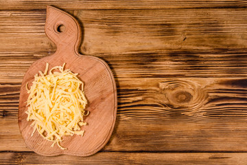 Cutting board with grated cheese on wooden table. Top view