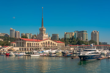 Fototapeta premium Sea port in summer. Many different yachts and boats stand at the marina. Yachtsmen and travelers are preparing to sail in the sea. In the background of the building of the seaside city.