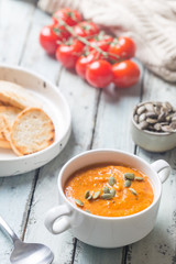 Healthy tomato soup in a white bowl with cream and pumpkin seeds