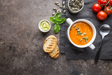 Healthy tomato soup in a white bowl with cream and pumpkin seeds, top view
