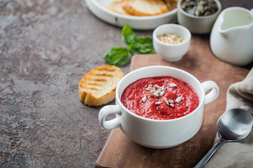 Red Beetroot mashed soup with cream and sunflower seeds in a white bowl.