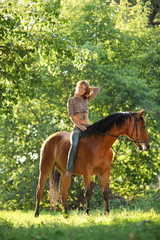 Beautiful cowgirl bareback ride her horse in woods glade at sunset