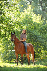 Fototapeta premium Beautiful cowgirl bareback ride her horse in woods glade at sunset
