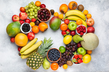 Heart made from healthy colorful fruits, strawberries raspberries oranges plums apples kiwis grapes blueberries mango persimmon pineapple on the white table, top view, copy space, selective focus