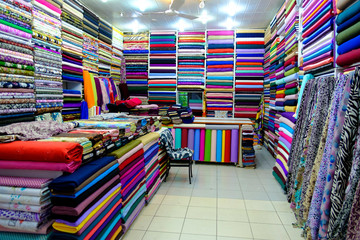 Rolls of fabric and textiles for sale stacked on shelves in shop,View of cloth rolls of different colors and patterns on shelves in fabric store 