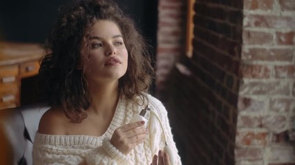 Young beautiful confident fashionable woman using, holding luxury perfume in vintage white glass bottle with pump. Model wearing warm winter knitted sweater - Powered by Adobe