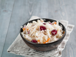 Traditional russian appetizer sauerkraut with cranberry and carrot in dark craft plate on gray rustic wooden table. Fermented cabbage. Russian cuisine and russian kitchen.