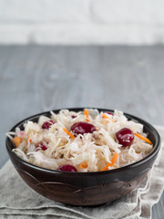 Traditional russian appetizer sauerkraut with cranberry and carrot in dark craft plate on gray rustic wooden table. Fermented cabbage. Russian cuisine and russian kitchen.