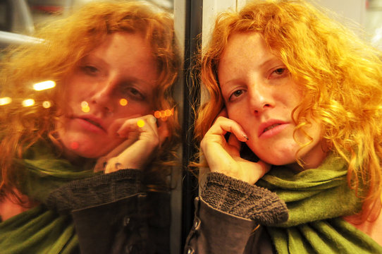 junge rothaarige sch&ouml;ne sexy Frau sitzt nachdenklich tagtr&auml;umend in einer fahrenden S-Bahn das Portrait spiegelt sich m Fenster