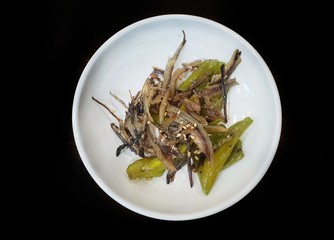 Korean food style, Top view of anchovy stir fried with green pepper, sprinkled with sesame seeds on white plate isolated on black background, Myol chee khum is korea traditional