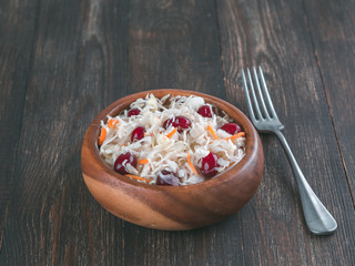 Traditional russian appetizer sauerkraut with cranberry and carrot in wooden bowl on brown rustic wooden table. Fermented cabbage. Russian cuisine and russian kitchen.