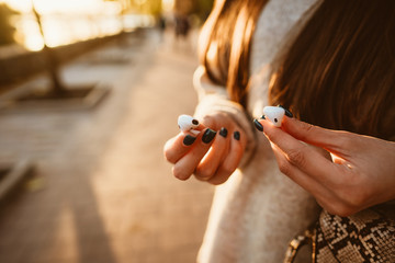 Beautiful young girl holding wireless headphones in park
