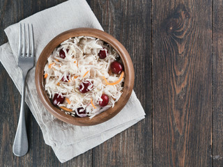 Traditional russian appetizer sauerkraut with cranberry and carrot in wooden bowl on brown rustic wooden table. Fermented cabbage. Russian cuisine and russian kitchen. Top view or flat-lay.