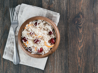 Traditional russian appetizer sauerkraut with cranberry and carrot in wooden bowl on brown rustic wooden table. Fermented cabbage. Russian cuisine and russian kitchen. Top view or flat-lay.