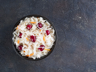 Traditional russian appetizer sauerkraut with cranberry and carrot in dark bowl on black cement background. Fermented cabbage. Russian cuisine and russian kitchen. Top view or flat-lay. Copy space.