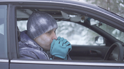 Frozen man sitting in the car and warm his hands