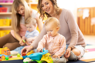 Fototapeta premium Moms with babies playing on the floor. Moms with daughter and son playing in car
