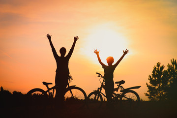 Silhouette of happy mother and son biking at sunset