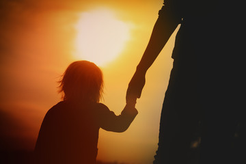 silhouette of little girl holding parent hand at sunset