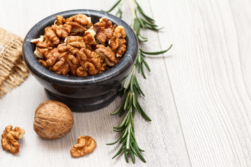 Walnuts in stone bowl and rosemary on a wooden background.
