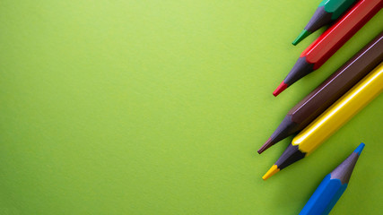 Colored pencils on the table. School supplies on green background. View from above with copy space