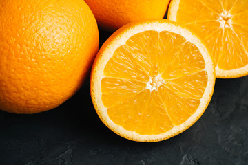 Orange, ripe citrus fruits and round slice on a black, textured background